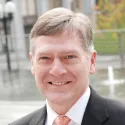 Image of Pete Holmes wearing a black suit, white button-down shirt and coral patterned tie