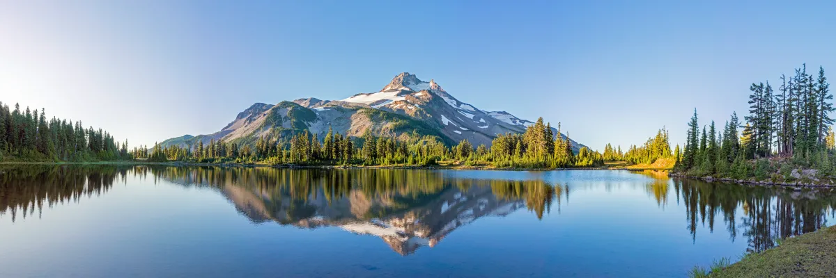 Image of a mountain reflected in a lake surrounded by greenery and trees