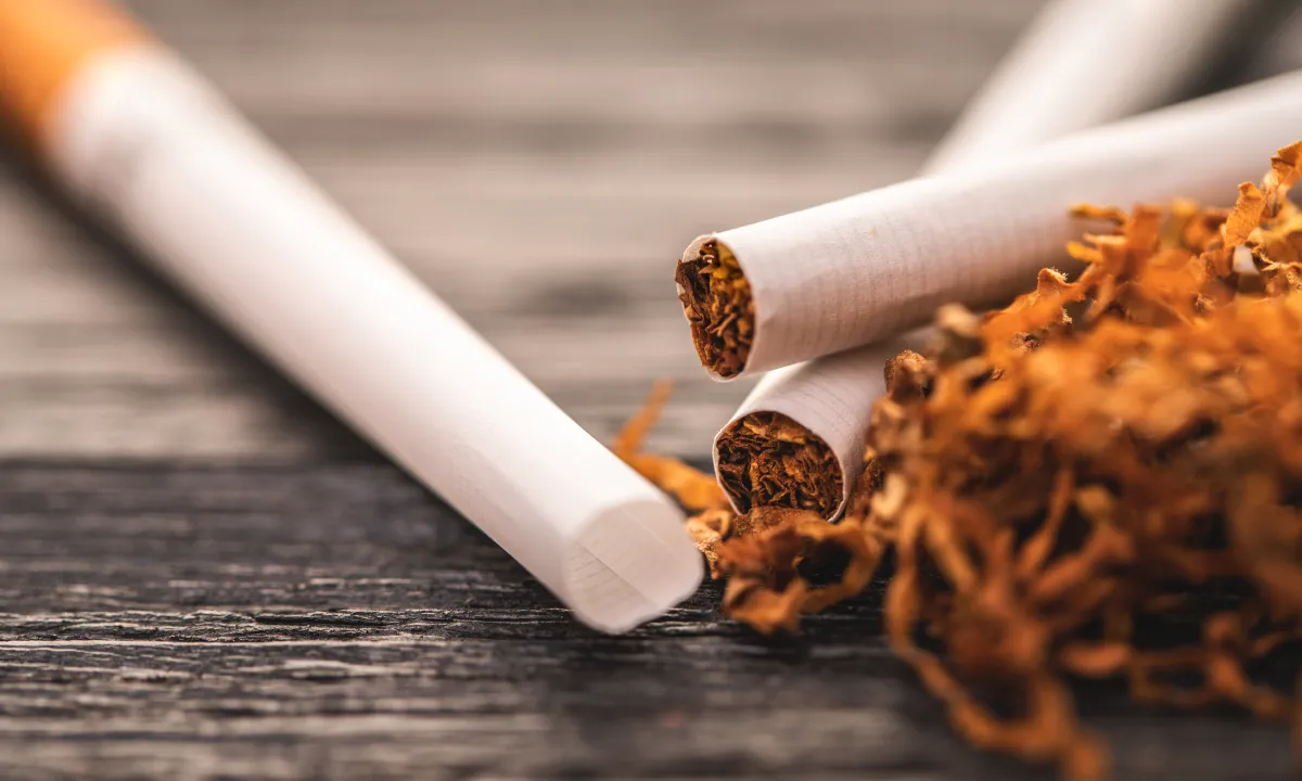 close-up image of rolled cigarettes and loose tobacco on a wooden background