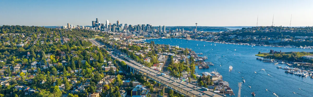 overhead image of I-5 highway in Washington, with water of the south sound on the right, trees and greenery on the left, and the Seattle skyline in the distance