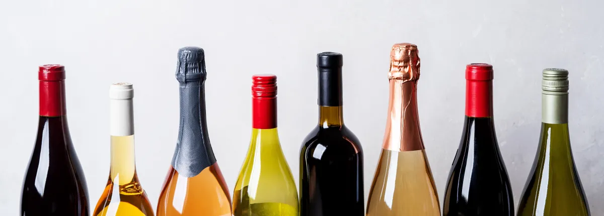 tops of eight wine bottles in varying shades of green and red, with red, white, silver, pink, and blue colorful foil