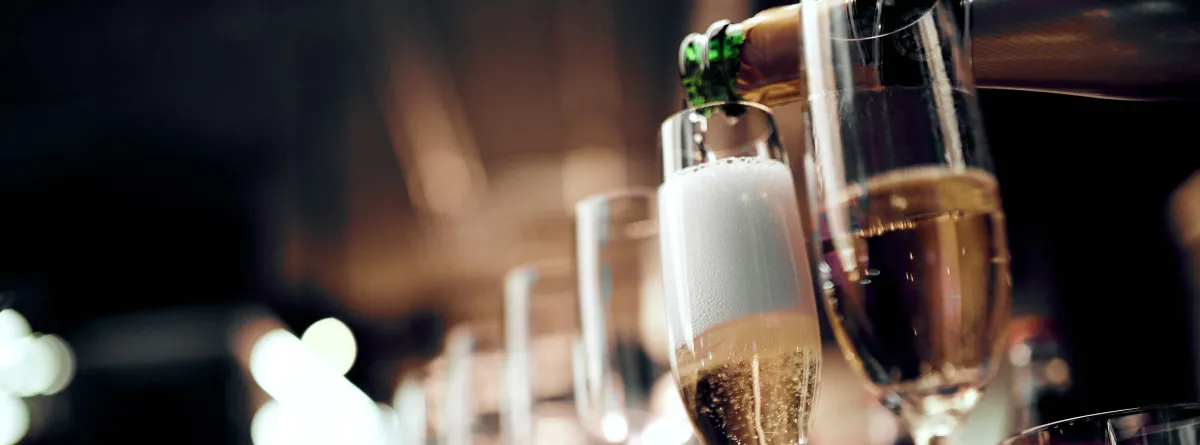 close-up image of a line of champagne glasses being filled from a green champagne bottle