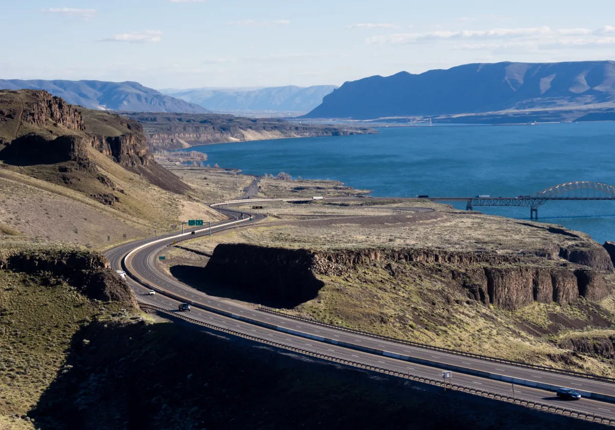 image of a highway winding along a coast with hills and mountains in the background