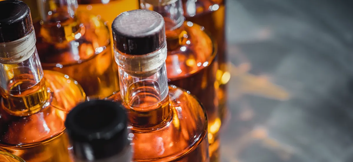 close up image of lined up bottles of whiskey on a grey background