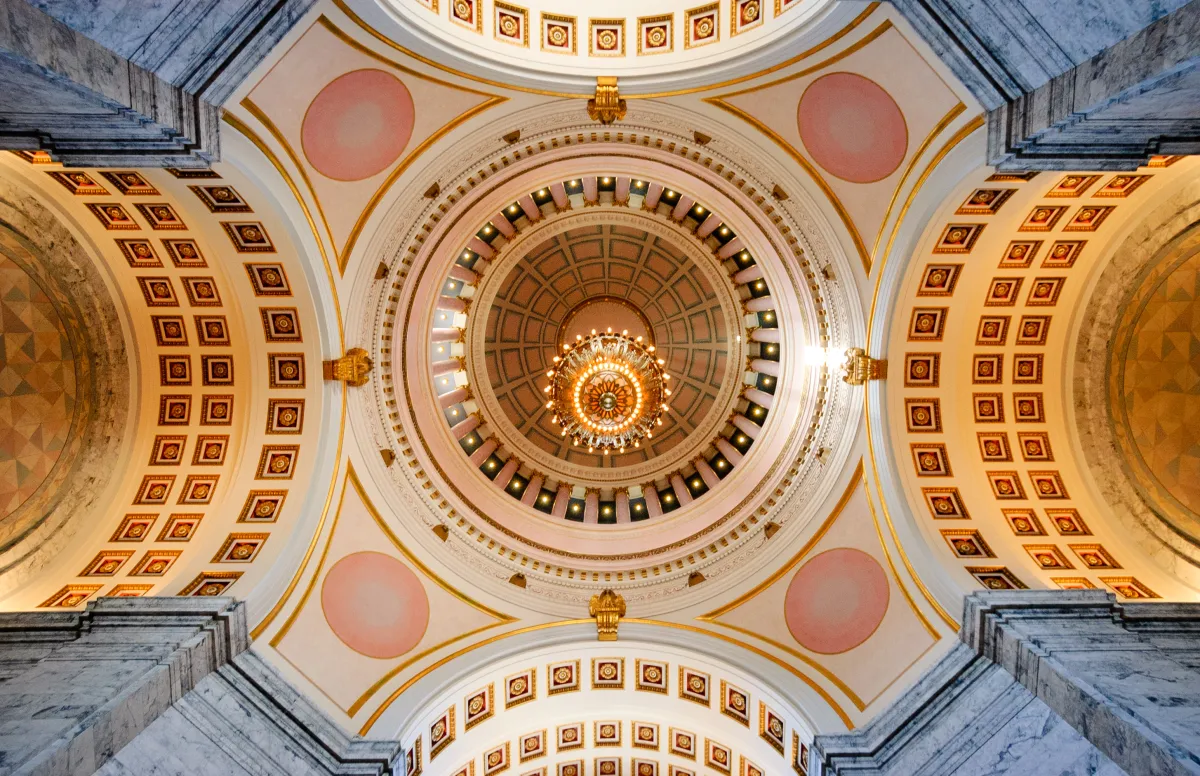 image looking up at the Olympia capitol building rotunda from the interior, a gilded ceiling with chandeliers and four arches