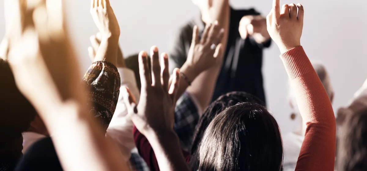 group of people sitting in a room with raised hands