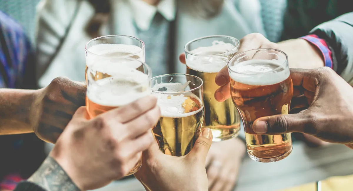 five peoples' hands clinking pint glasses filled with an amber liquid