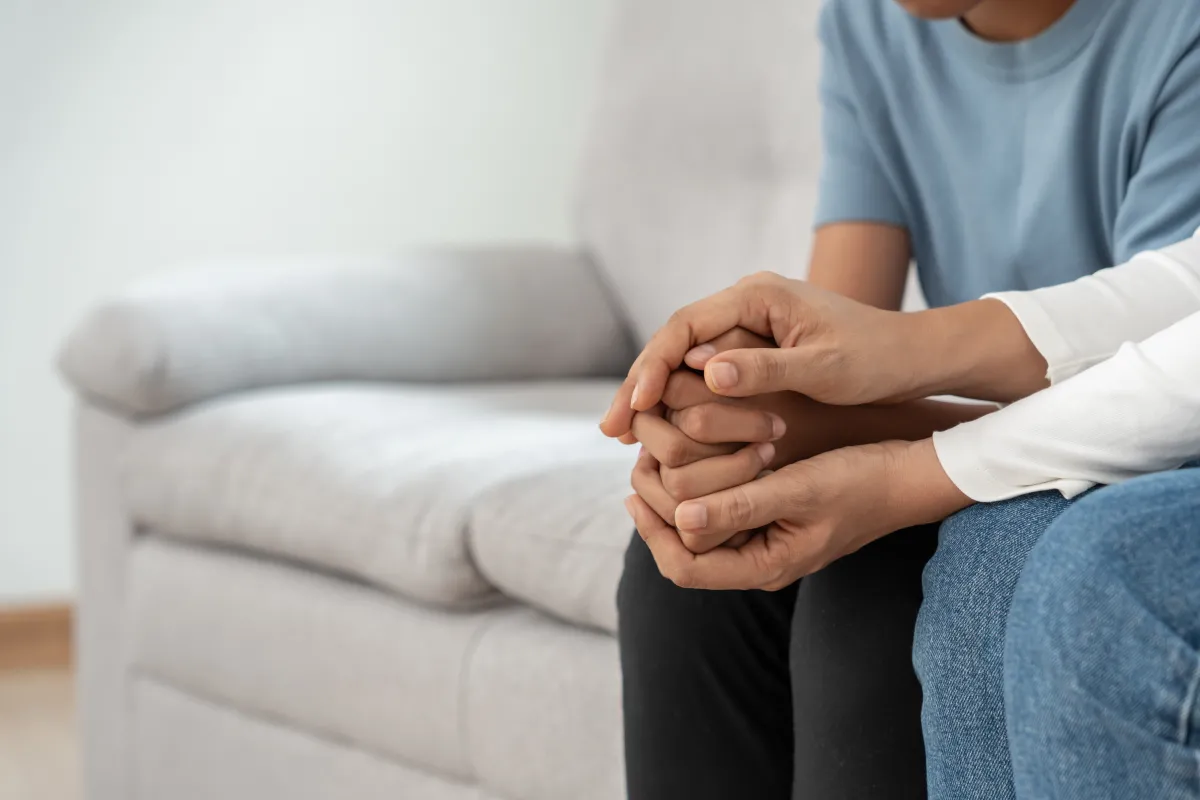 adult holding the hands of a young person sitting on a couch together