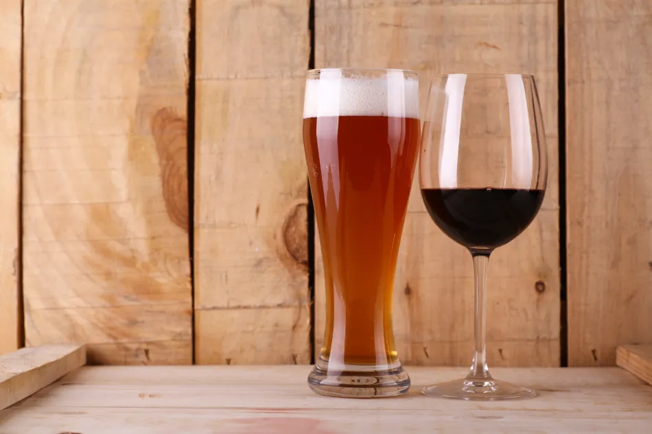 a tall glass of beer and a glass of red wine sitting next to each other on a wooden background